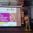 A speaker presents at a café with a colorful slide about body health on a screen.
